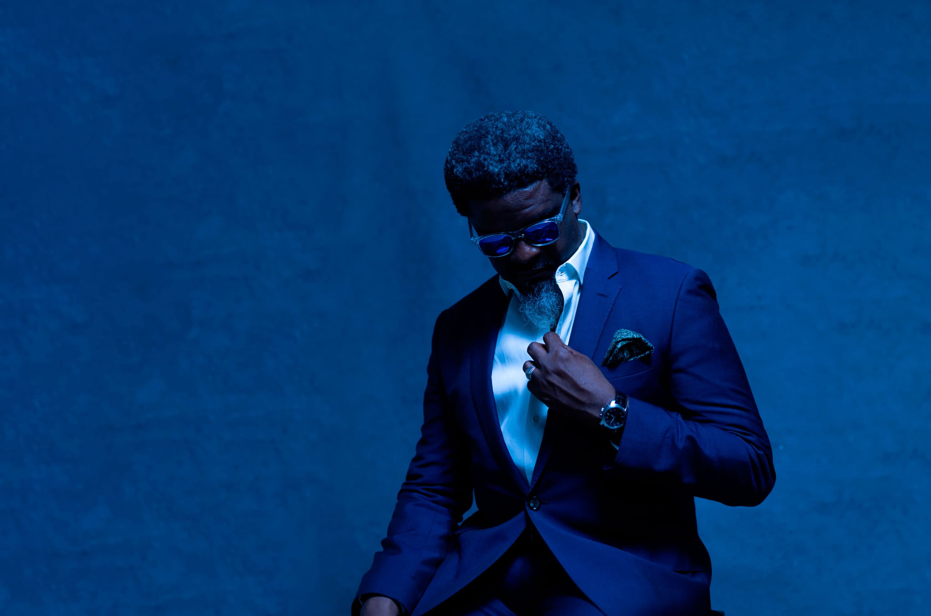 Dele Balogun in a dark suit against a blue backdrop